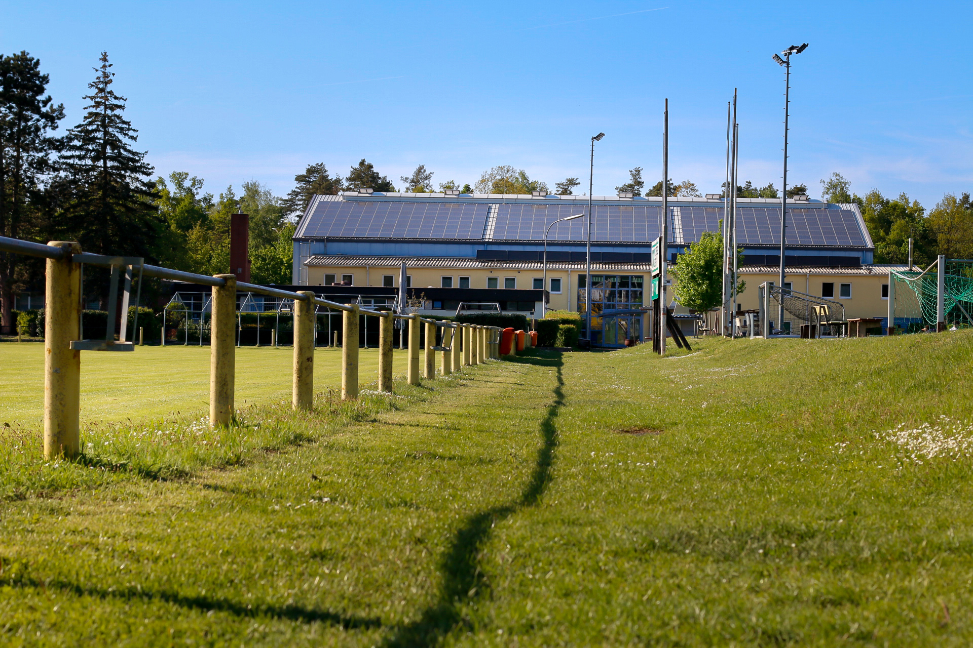 Das Foto ist knapp über einen Fußballplatz fotografiert. Im Hintergrund ist eine Sporthalle zu sehen